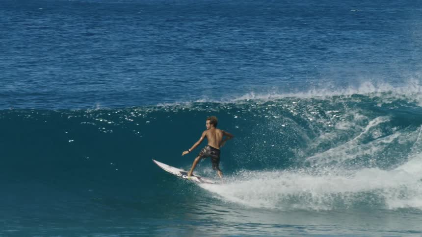 A surfer stands up on his surfboard and surfs across a wave before falling into the ocean