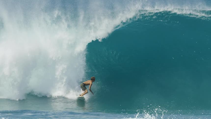 Youth paddles down swelling wave and stands on board as other surfers paddle the other way