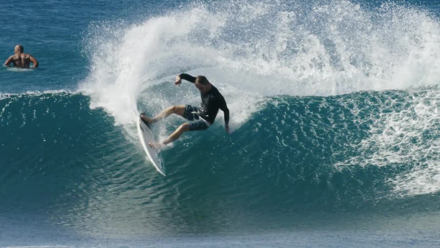 The wave surfer is riding crashes as others sit in water in the background