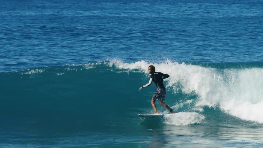 Male surfer with black wetsuit and shorts rides and jumps wave