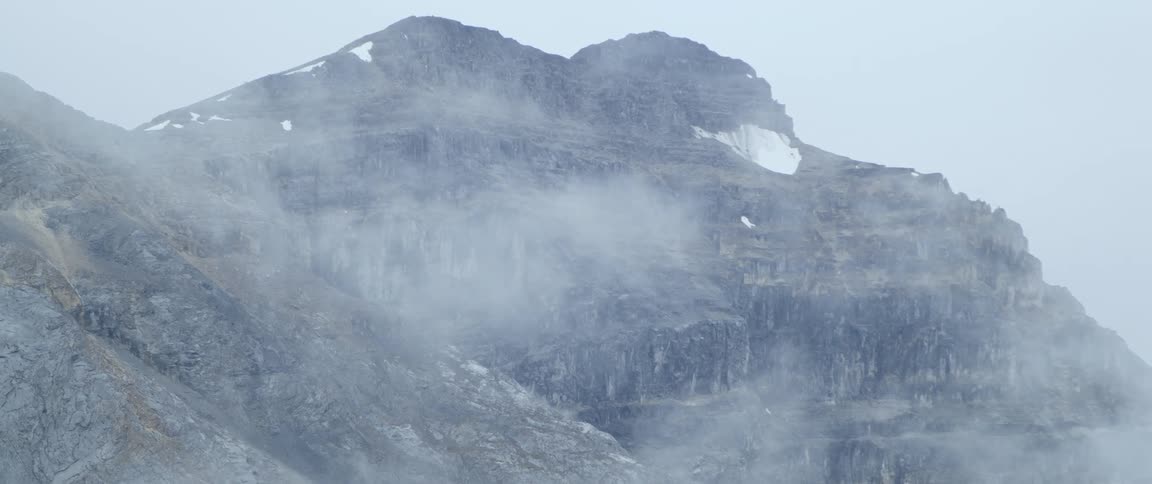 A mountain ridge shrouded in fog during the day