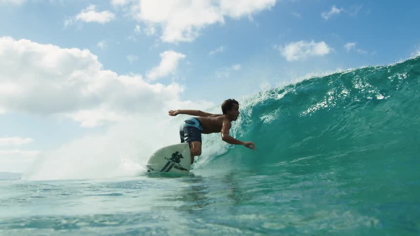 A man stands up on his surfboard to ride an ocean wave