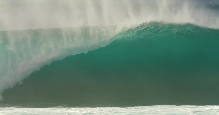 A large wave knocks multiple surfers off their surfboards in the ocean