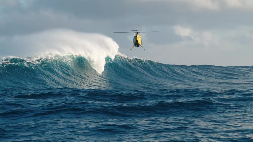 A helicopter tries to rescue people on a raft in the ocean as a giant wave passes through