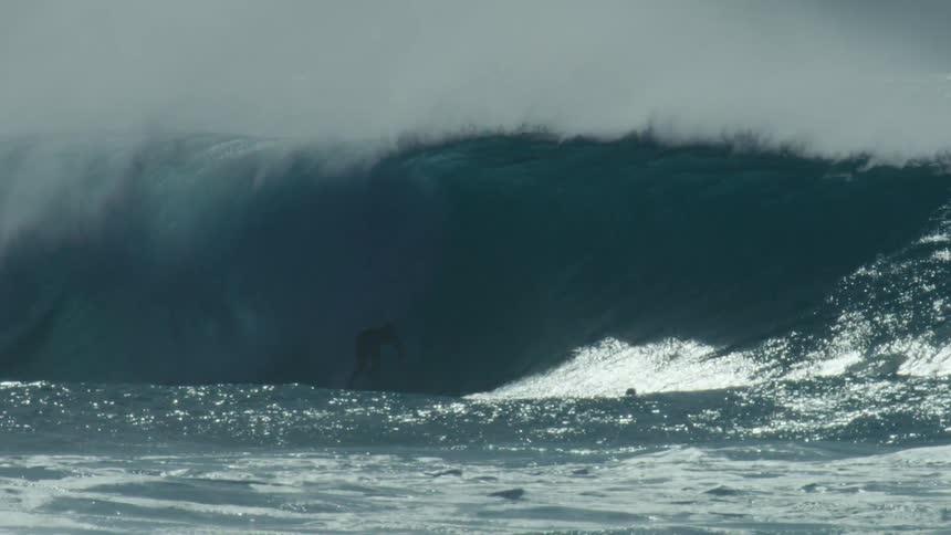 People swim and ride surfboards as a large wave rises in the ocean