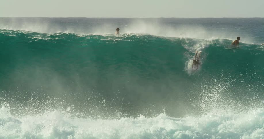 A group of surfers ride over a large wave