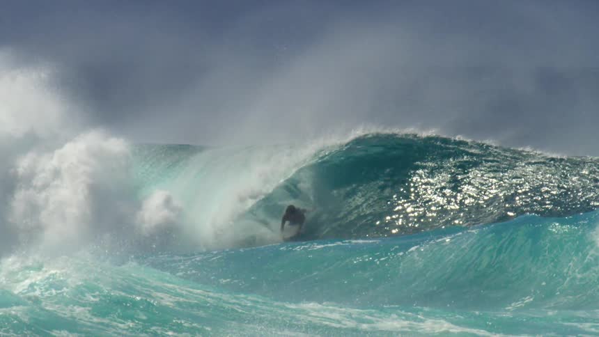 A surfer is riding a huge blue wave as it rolls overhead splashing and goes over him
