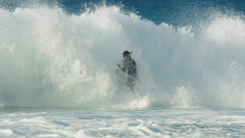 Surfer rides wave making a short leap before turning then falling as wave crashes around him