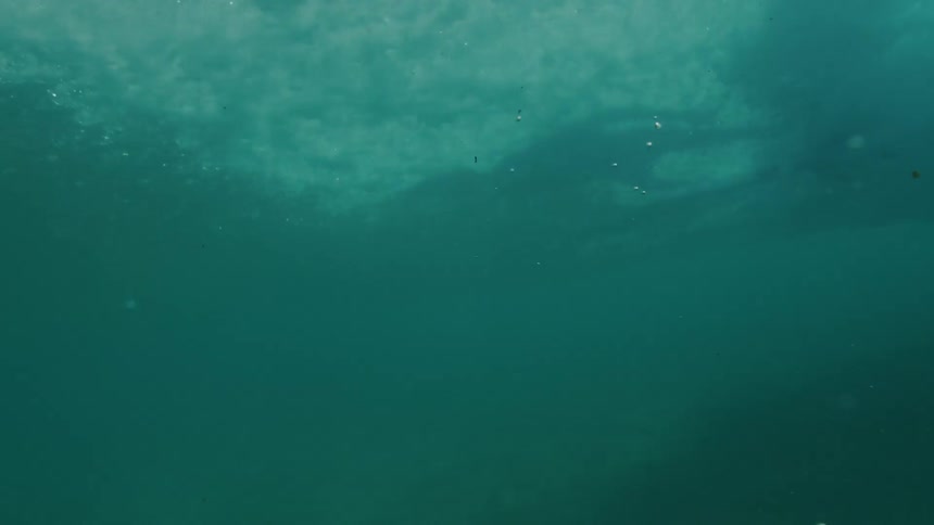 Surfboard cuts through ocean near murky seafloor