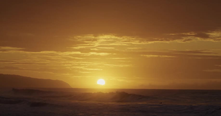 Waves roll in under an orange sky as the sun sets on the horizon