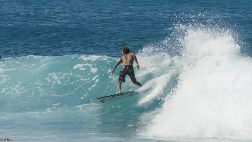 A surfer is riding a big blue wave as water splashes behind him