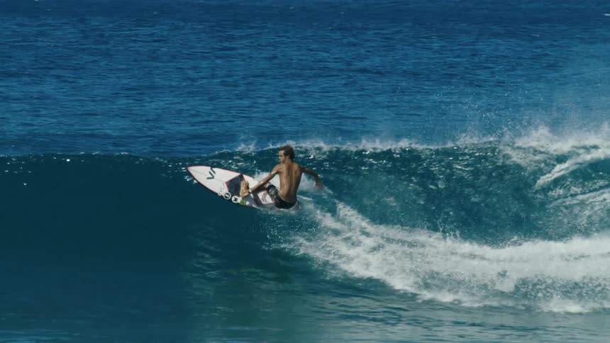 Young man riding a white surfboard over a big wave in the ocean