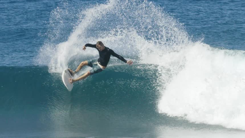 Male surfer with wetsuit and shorts rides ocean wave
