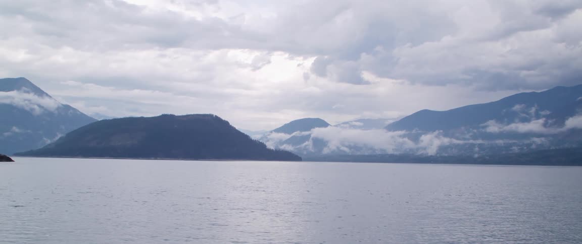 River water is flowing and there are mountains along the coast under a cloudy sky