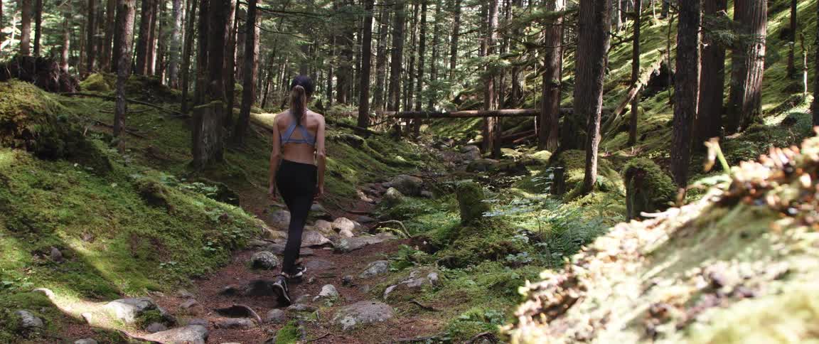 Woman with ponytail cap sports bra black leggings and sneakers walks in the forest
