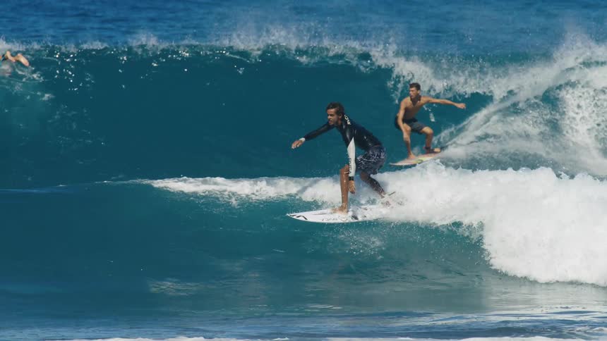 Surfers with wetsuit and shorts ride waves on surfboards