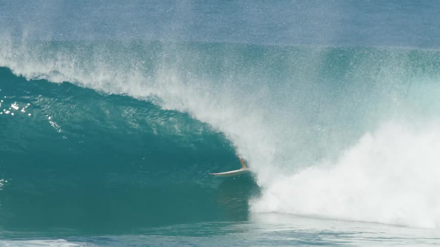 Surfer ride through barrel of wave kicking up foam as other surfers paddle on their boards