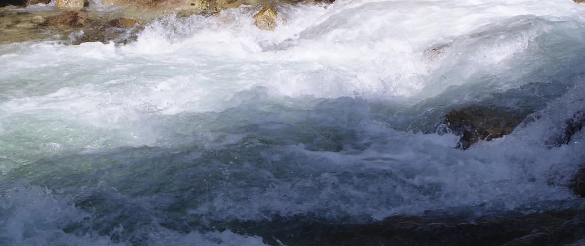 The sun shines on rapids splashing as they roll over rocks