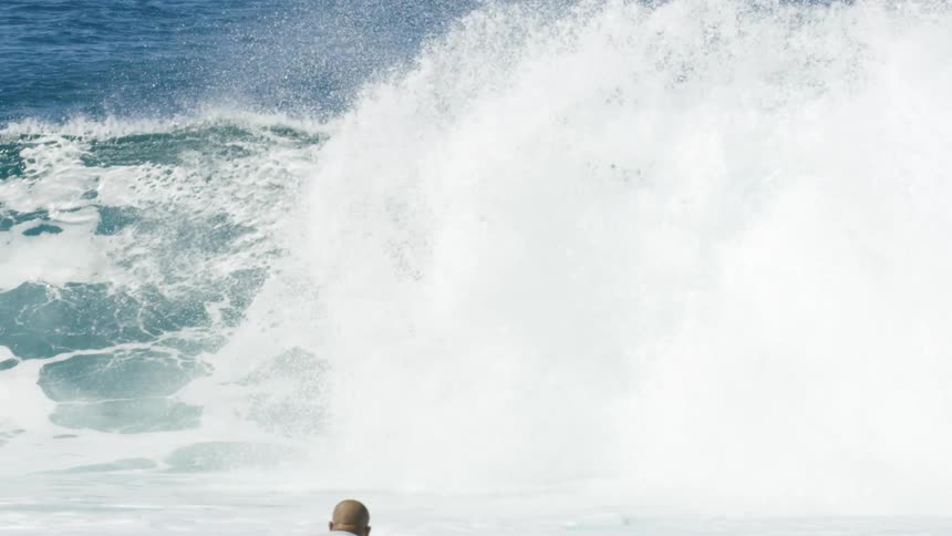 Man rides surfboard along wave passing other surfers lying on their boards