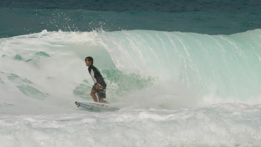 A man laughs as a large wave goes over his head as he surfs and then he flies off his board