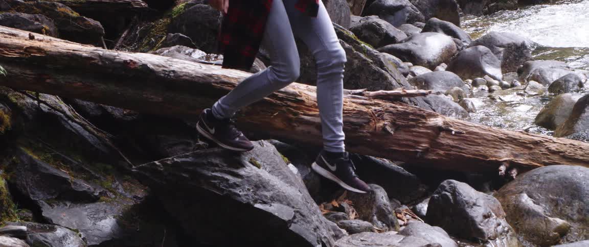 A person climbs over the rocks and log in the stream