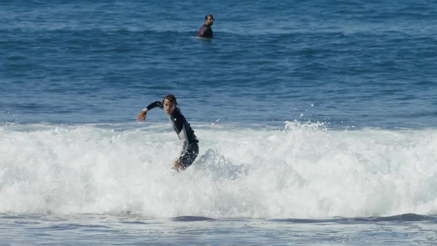 A man on a surfboard rides a wave in then falls off