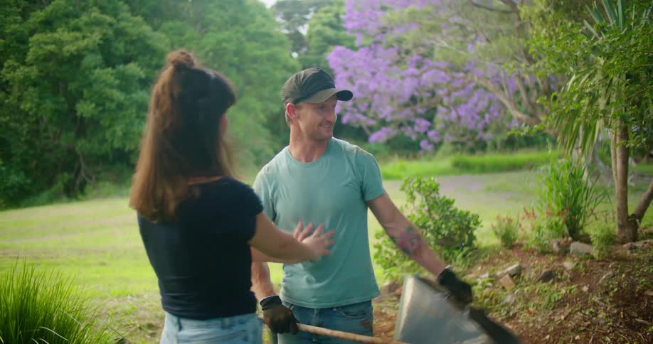 Man carrying rake and flexible bucket walks up to woman and kisses her