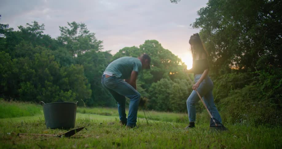 A woman rakes a large yard and a man picks up the pile