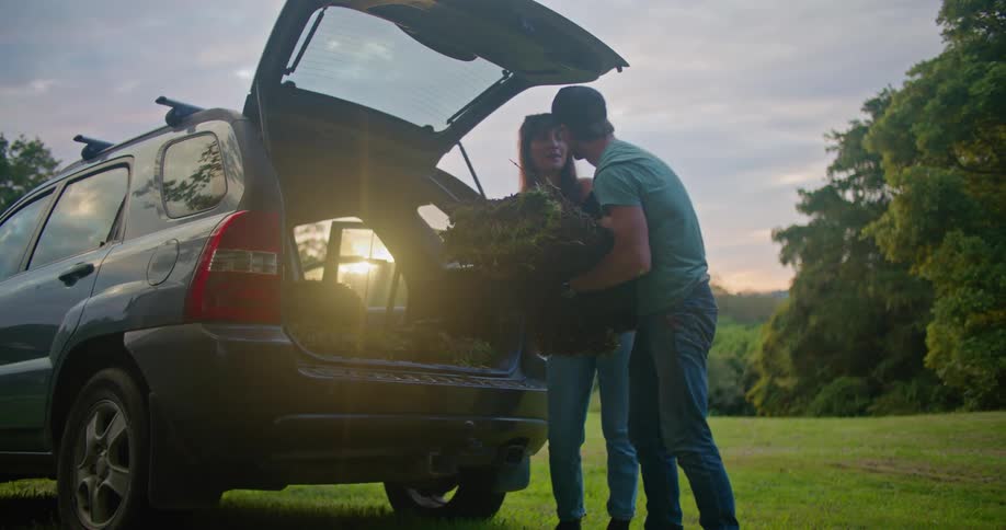 A man and a woman are taking sod out of the back of their automobile