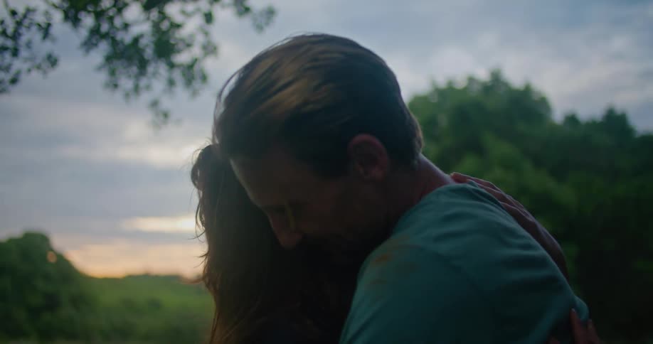Man with turquoise t shirt cuddles woman making out in the countryside at sunset