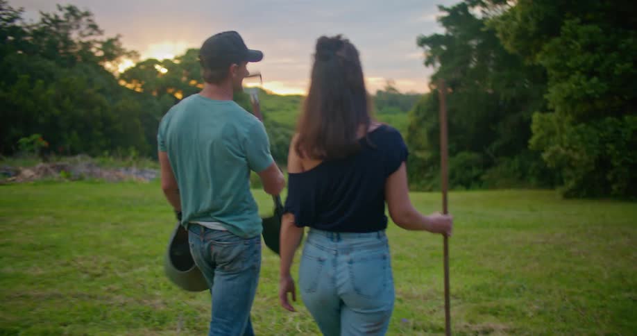 A man and woman carry a shovel and rake in a large rural lawn
