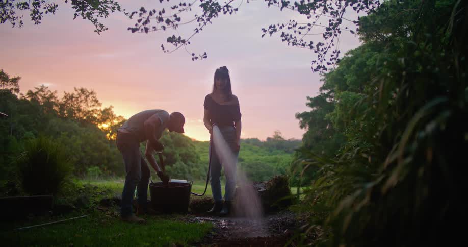 A woman hoses a lawn with a man digging with a shovel beside her