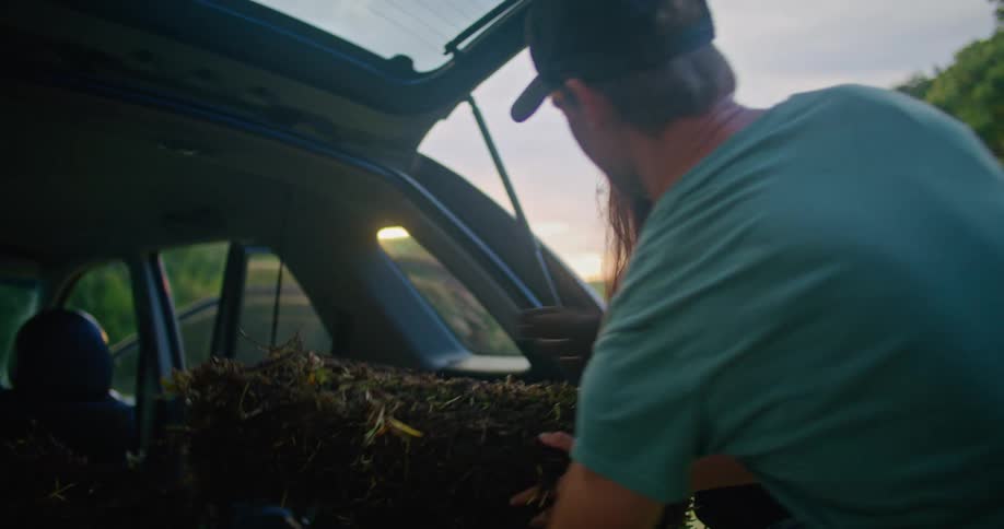 Man takes stack of grass segments from woman who unloaded them from back of vehicle
