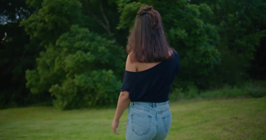 Woman with brown wavy hair black blouse and jeans talks on smartphone in the countryside at dusk