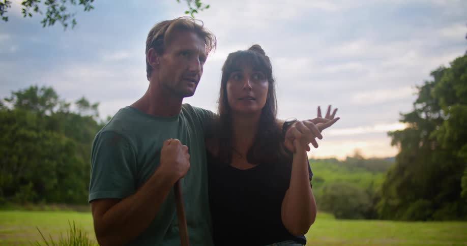 Man with turquoise t shirt holding woman with wavy brown hair and black blouse kissing and talking to each other in the countryside