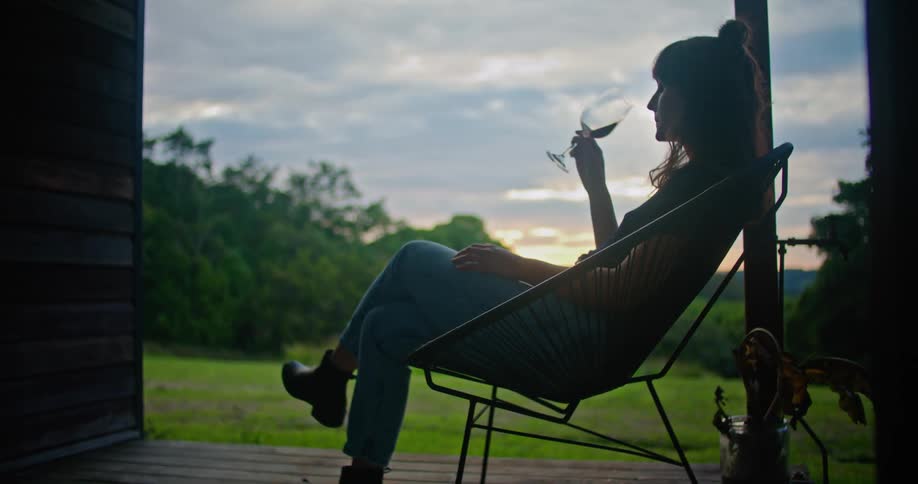 A woman sits in a chair outside sipping a glass of wine