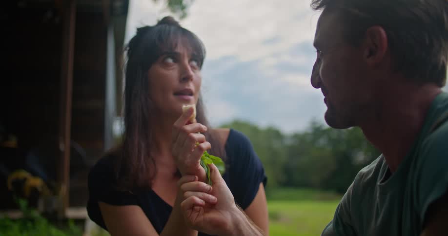 A man and woman kneel on the ground and share a fresh vegetable