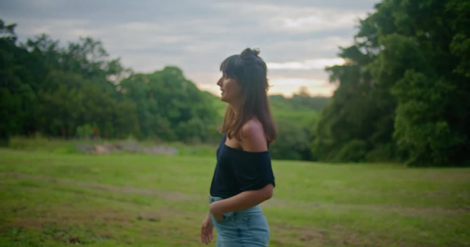 Woman with brown wavy hair black blouse and jeans kisses man with dark blue cap turquoise t shirt and jeans gardening in the field at dusk