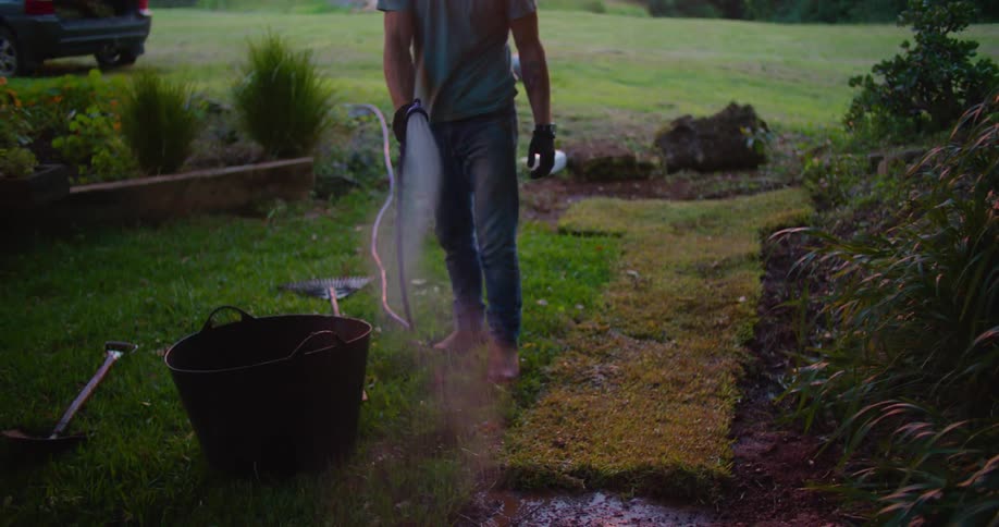 Man watering some newly planted sodding near a grass field