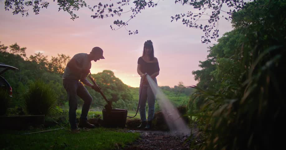 A woman sprays the hose as a man digs