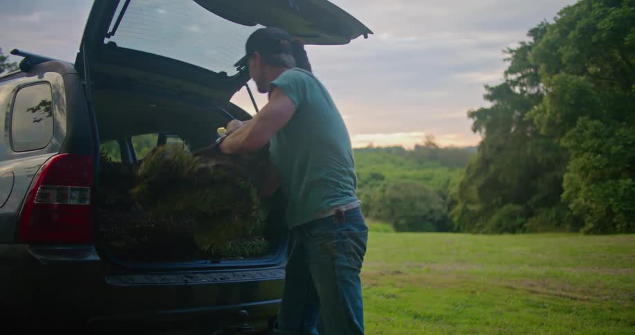 Man and woman unload turf segments from rear of vehicle with red sky on the horizon