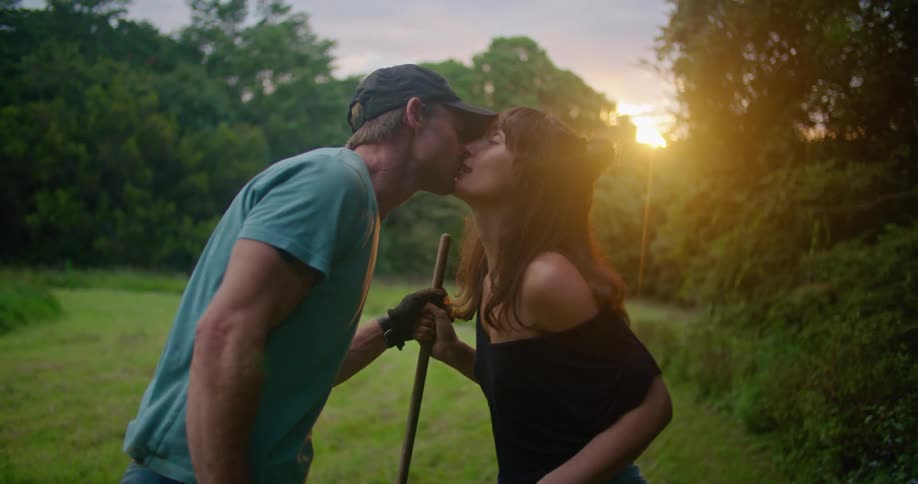 Couple rakes ground before kissing as sun shines from red sky
