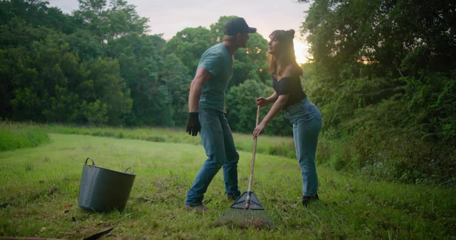 A man picks up leaves while his wife rakes and gives her a kiss