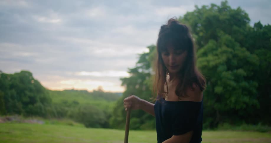 A woman uses a rake to clean up leaves on a large rural lawn