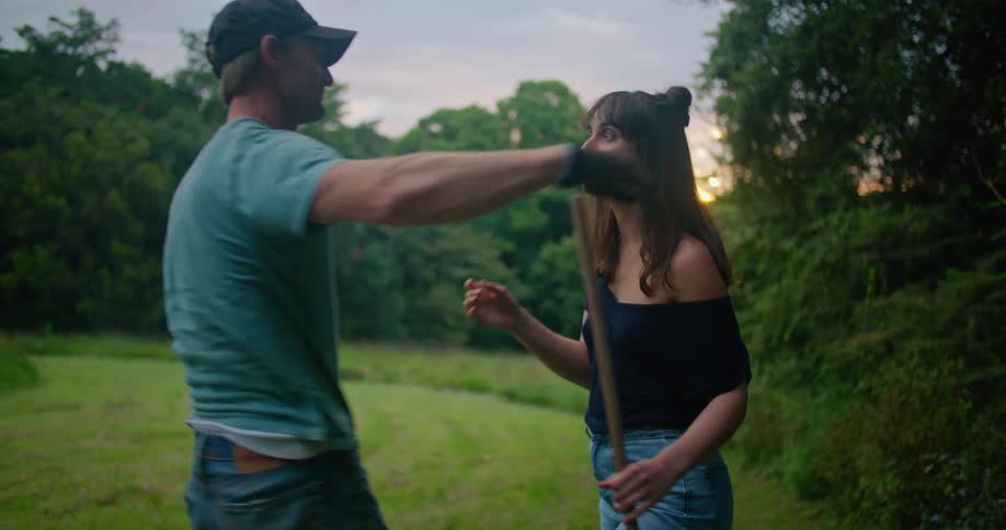 A woman rakes a rural lawn and a man wraps his arm around her