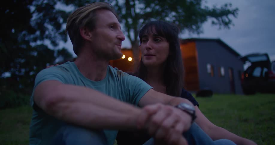Two people are sitting in the grass together at dusk