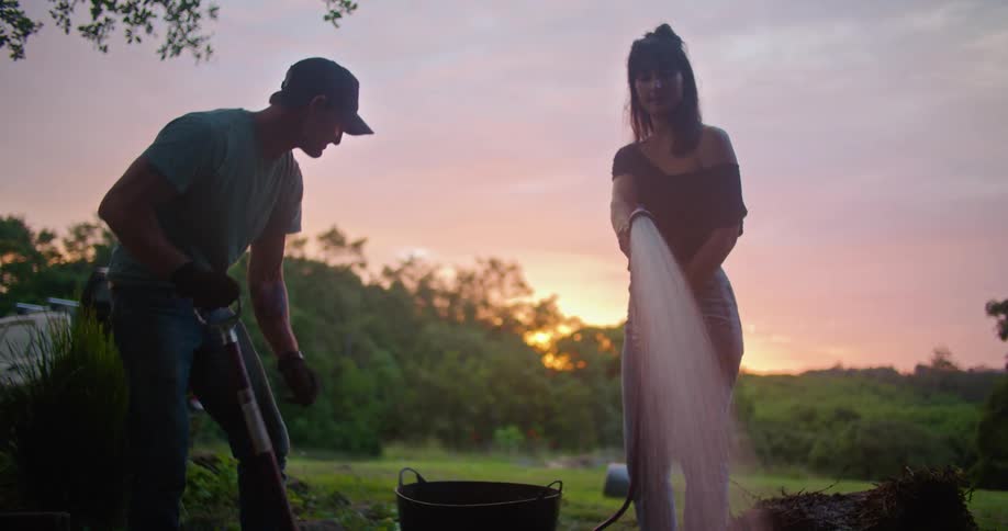 A woman sprays a hose in a rural yard with a man using a shovel beside her