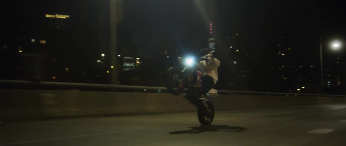 A man does a wheelie while driving a motorcycle down a street at night