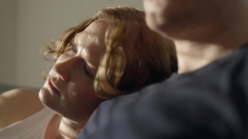 A woman rests her head on the shoulder of a man next to her looking sad and contemplative