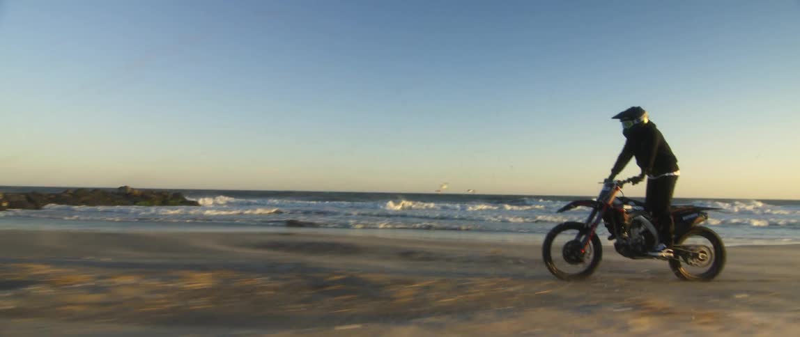 A man speeds across a beach on a motorcycle